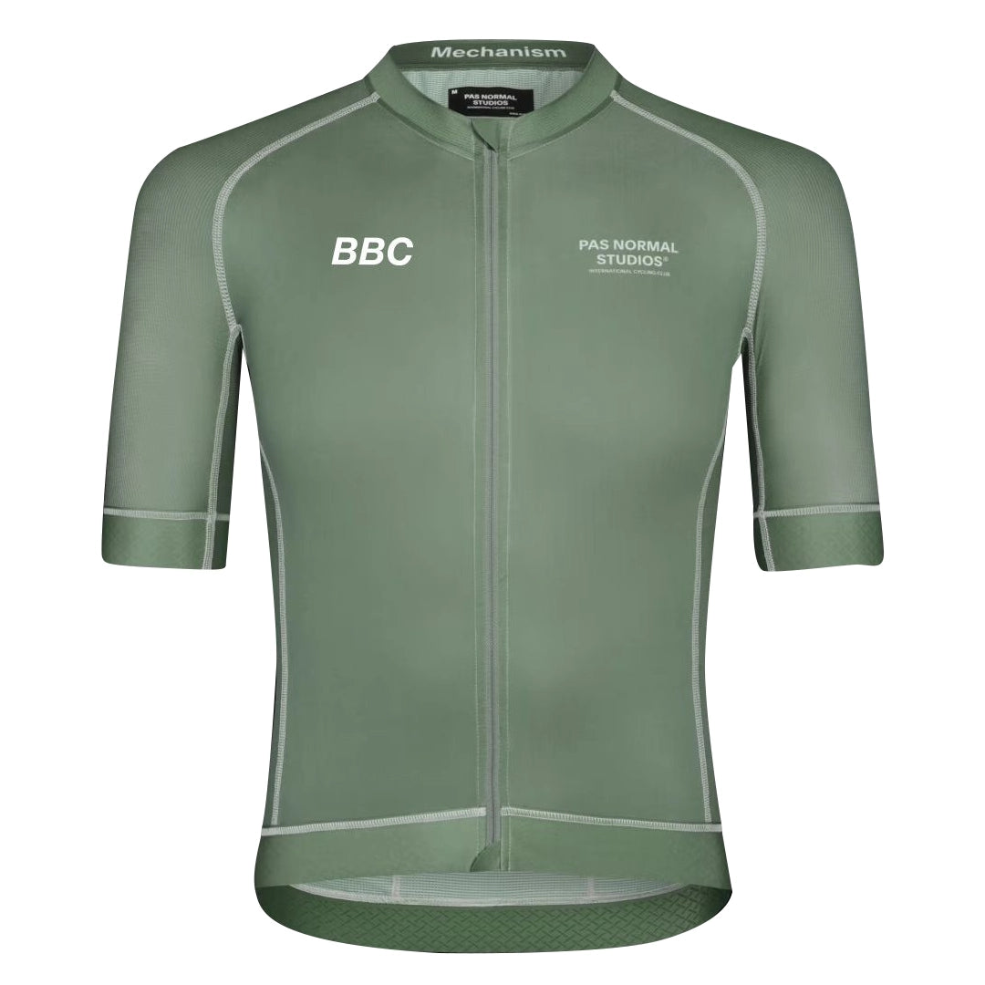Front view of a khaki green cycling jersey with white piping. “PAS NORMAL STUDIOS” is printed on the chest along with “BBC” and “Mechanism” on the collar.