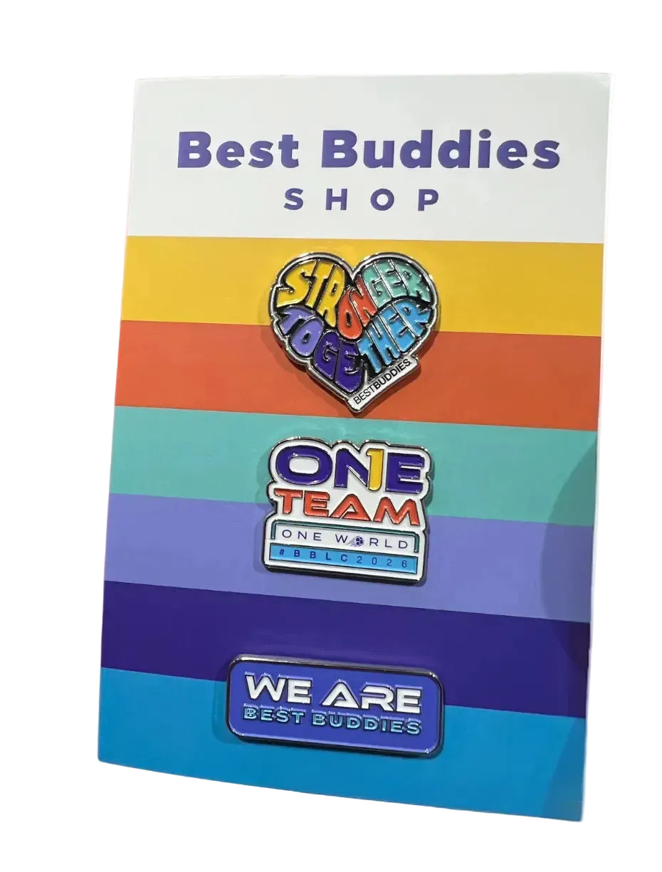 A set of three colorful enamel pins displayed on a white backing card with rainbow stripes and the text 'Best Buddies Shop.' The pins read 'Sit Together,' 'One Team One World Best Buddies,' and 'We Are Best Buddies.