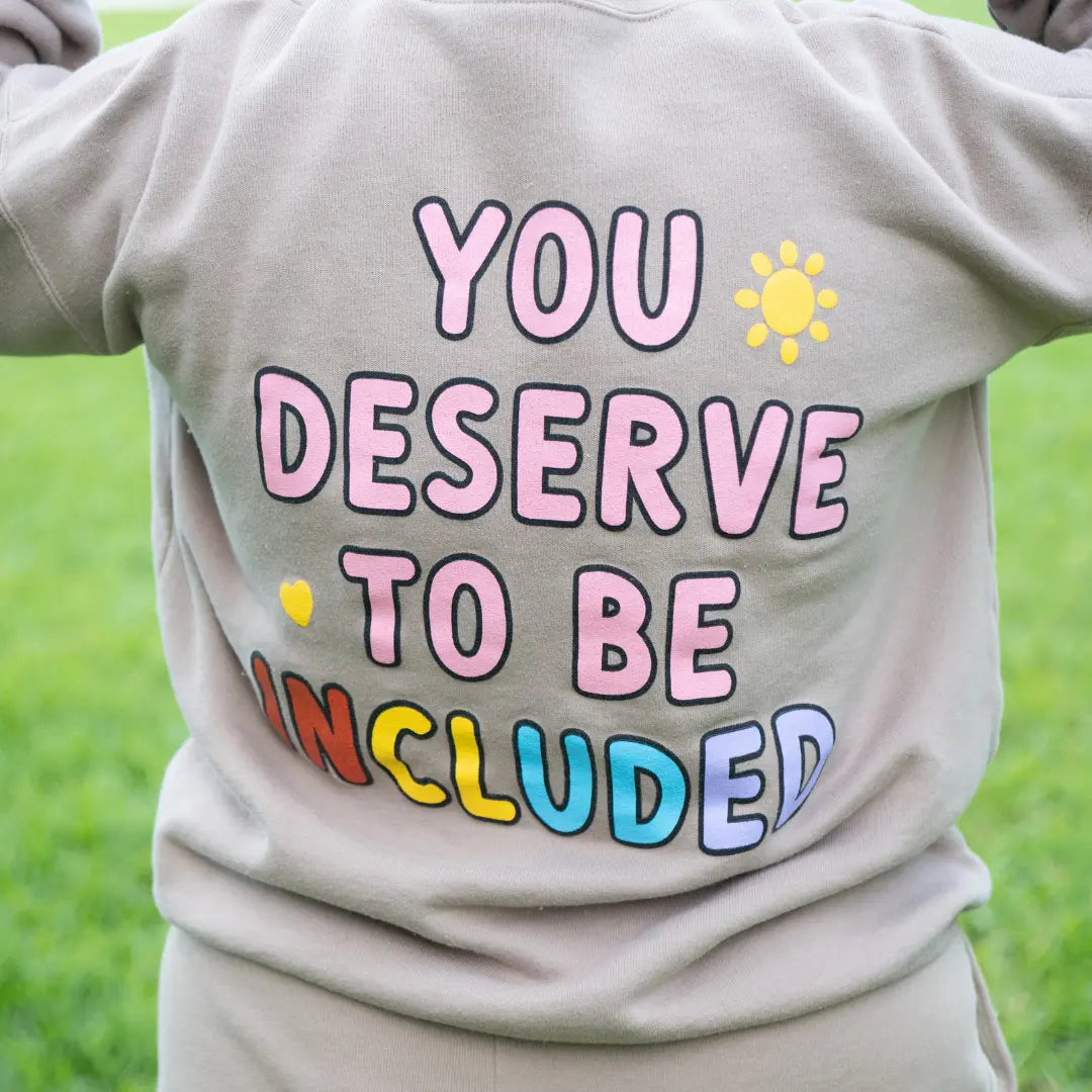 Best Buddies Crewneck beige Sweatshirt with ‘You Deserve to Be Included’ message printed in colorful letters on the back.