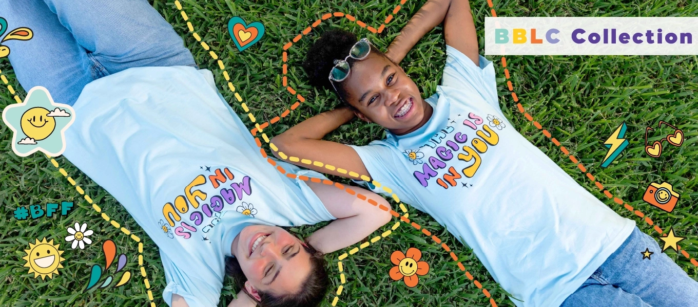 Two smiling individuals lying on the grass wearing matching t-shirts that read 'Magic is in you'. The image is surrounded by colorful, playful doodles and text that says 'BBLC Collection."